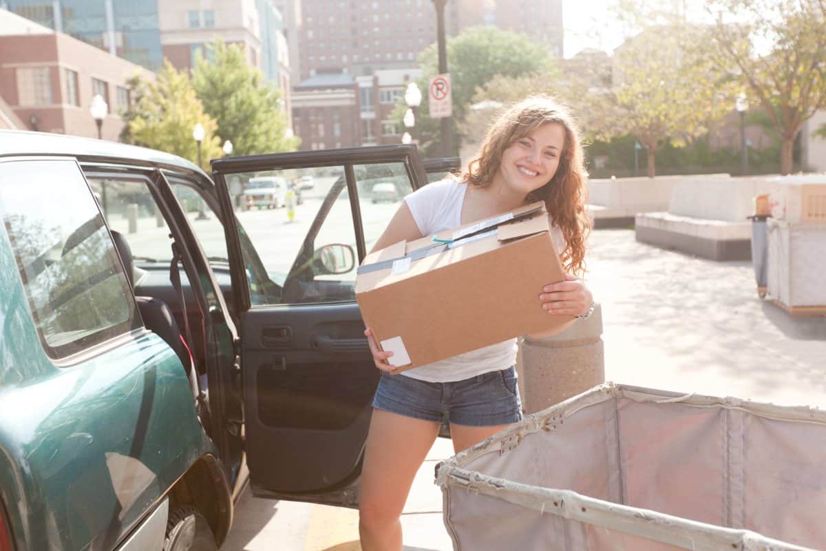 young person carrying a moving box to put into a car