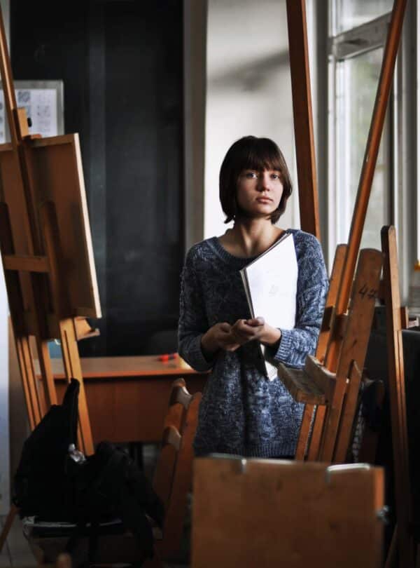 persona holding a drawing tablet standing next to an easel.