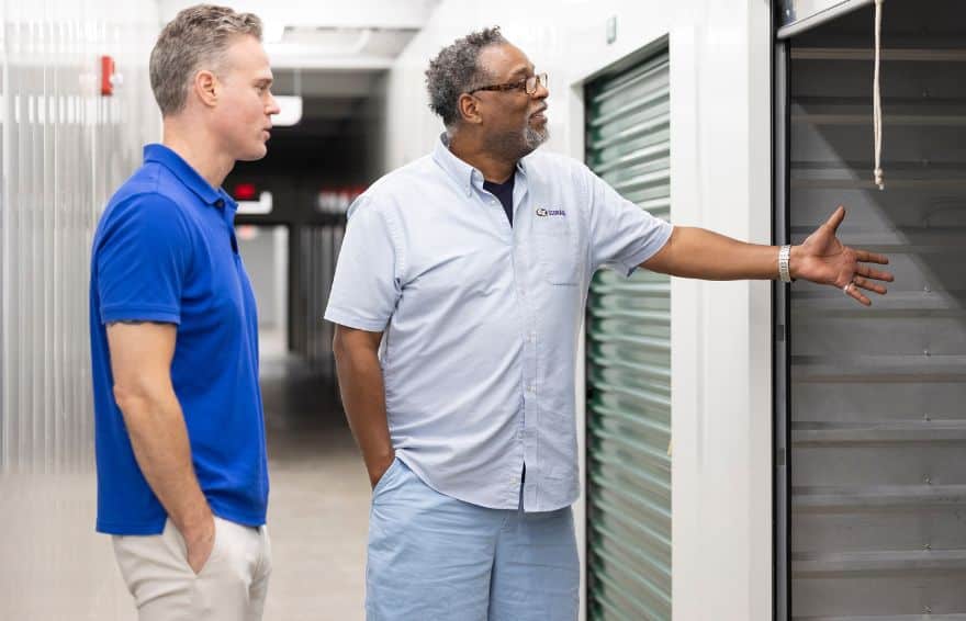 two men standing in front of an open self storage unit, one of the men explaining the size of the unit to the other using a hand gesture