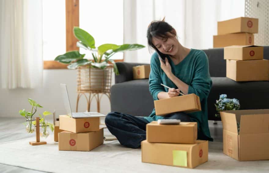 woman holding a phone to her ear as she sits on the floor holding a cardboard box